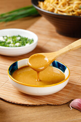 Sesame oil dripping from wooden spoon with Asian noodles and fresh ingredients