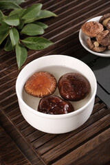 Fresh shiitake mushrooms soaking in white bowl with dried mushrooms on bamboo background for cooking ingredients