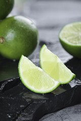 Fresh Green Lime Wedges and Whole Limes on Dark Stone Surface for Cocktails and Cooking