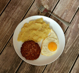 Beefsteak with fried egg and mashed potatoes in a round ceramic plate on a wooden table, rowan fork.