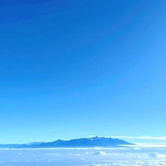 Obraz premium Distant mountain range peaks through a sea of white clouds, all set against a vast, clear expanse of bright blue sky