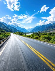Fototapeta premium Long asphalt road stretching toward distant blue mountains under a partly cloudy, bright blue sky on a sunny day