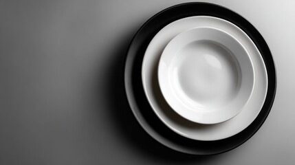 Close-up of stacked white and black ceramic plates arranged in descending size order on a dark surface with soft lighting and minimal shadow for a modern tableware display