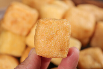 Hand holding golden fried tofu cube showing crispy texture and delicious bean curd preparation for...