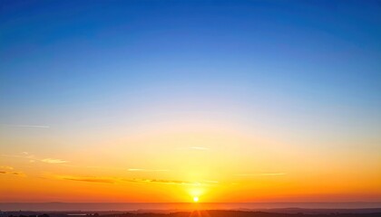 Radiant sunrise paints the horizon with gold and orange hues merging into a clear blue sky. A serene landscape awakens in soft morning light