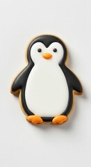 Naklejka premium A charming, detailed penguin-shaped cookie, expertly decorated with white and black icing, and orange feet, sits on a plain white surface.