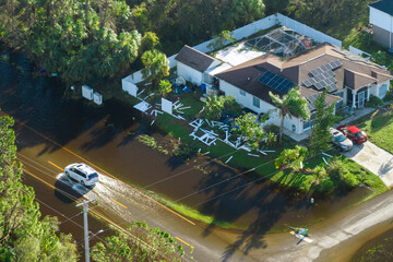 Flooded Florida road with evacuating cars and surrounded with water houses in suburban residential area. Consequences of hurricane natural disaster