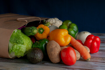 Assortment of vegetables coming out of a paper bag like products shared at the market on a wooden table side view grocery