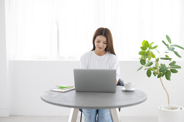 Young woman working on laptop at home in bright minimal interior