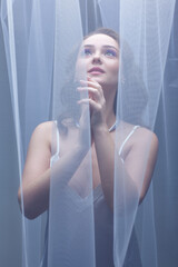 Portrait of a young female covered with veil. Woman is dressed in a peignoir and wears a necklace and earrings.