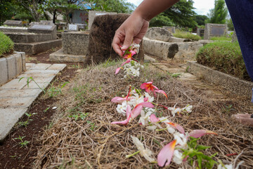 a man placing tropical flowers on an Indonesian grave, showing respect