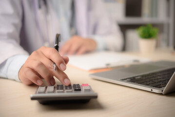 Doctor calculates medical billing at office desk with calculator laptop paperwork for insurance claim cost control finance management healthcare administration concept