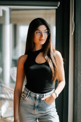 Young woman posing in a stylish outfit near a large window in a modern setting