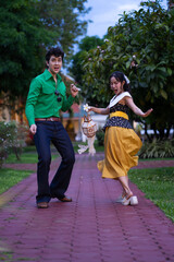 A young couple dressed in colorful retro-style outfits dancing together on a red brick walkway in a garden.
