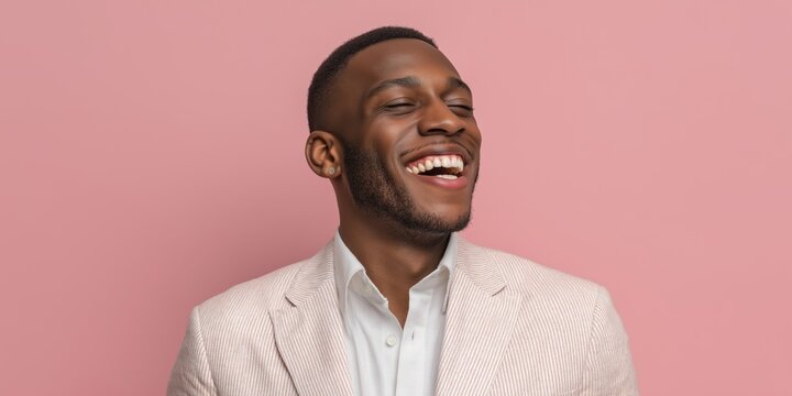 Smiling man in a light blazer poses against a pink background showcasing joy and confidence in a playful setting.