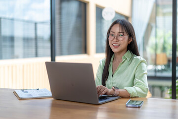 Young asian businesswoman smiling while working on laptop in a modern office