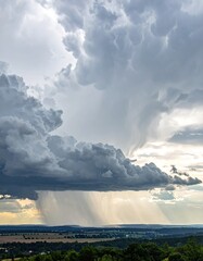 Dramatic storm cloud hangs heavily, casting rain down upon distant land. Rays of light pierce through the storm