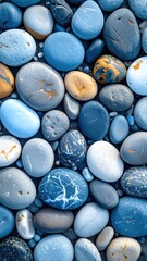 A textured close-up of smooth, varied-colored stones in shades of blue, gray, yellow, and white, arranged in a dense, natural pattern