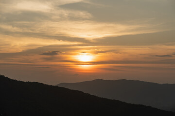 Serene Sunset Over Mountains with Orange and Yellow Skies, Clouds Silhouetted by Distant Peaks and Calm Atmosphere in Nature's Beauty