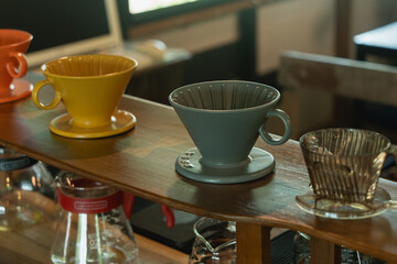 Colorful coffee drippers lined up on wooden counter in cozy cafe interior with blurred background showcasing a vibrant beverage preparation scene