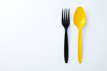A black plastic fork next to a yellow plastic spoon on a white