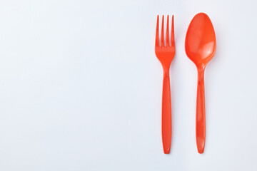 Red plastic spoons and forks are placed side by side on a clean white background, creating a simple and minimalist unbalanced composition