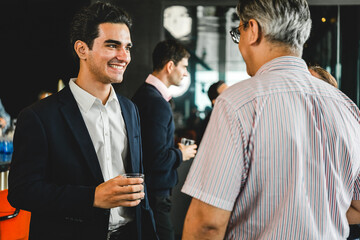 Two professionals chat at a networking reception, one holding a drink in a modern indoor venue, suggesting business conversation, connection, and casual corporate socializing.