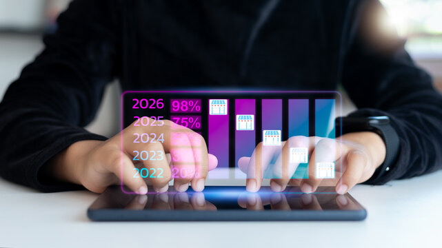 Hand using a tablet with a hologram bar chart showing business growth and market expansion from 2022 to 2026, digital transformation, startup success, and data analytics concept.