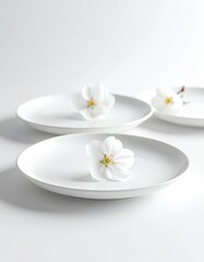 Three white plates, each adorned with a delicate white flower, set against a bright, clean, minimalist white background