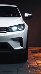 Cropped view of a modern white car, front lights glowing, parked on a shiny tiled floor against a dark blurred background