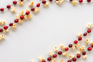 Decorative cranberry and popcorn garland arranged in elegant curves on white background, traditional Christmas craft decoration