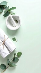 Relaxing spa scene eucalyptus leaves, a mortar with herbs, and rolled white towels tied with twine on a pale green surface