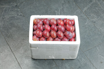 Fresh Red Plums in White Styrofoam Box Container on Stone Floor