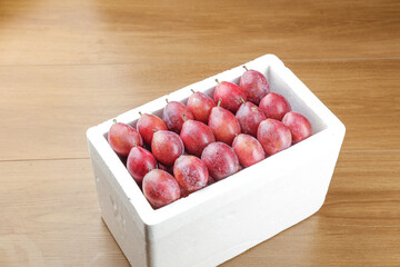Fresh Large Sweet Plums in White Container - Premium Imported Fruit Display on Wood Background