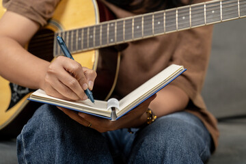 A creative young woman is enjoying her hobby, skillfully playing a guitar while concentrating on writing musical notes in her notebook. The scene captures the essence of music composition and artistic