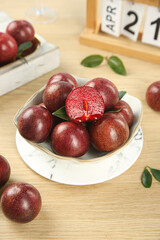 Obraz premium Fresh Red Plums in Bowl on Wooden Table - Healthy Organic Stone Fruit with Cut Half Showing Interior
