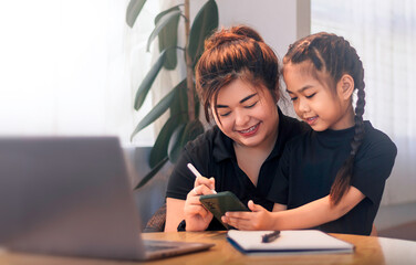 Mother and daughter sharing a learning moment while using a smartphone at home in the morning