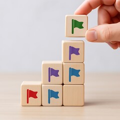 Hand stacking colorful flag blocks in ascending staircase pattern symbolizing growth and success