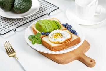 Healthy Avocado Toast with Egg and Blueberries Breakfast on Wooden Board