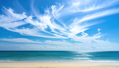 A beach scene showing brilliant blue water, sandy shore and a stunning sky with wispy cirrus clouds creating a peaceful and airy panorama