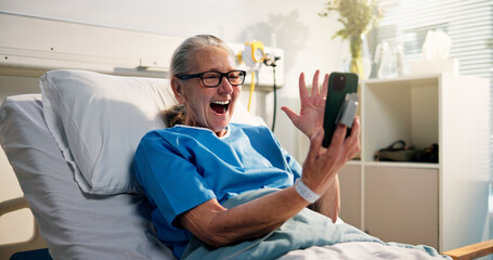Senior woman, phone and video call in hospital bed with wave, surprise or get well soon message. Person, smartphone and virtual contact on social media with rehabilitation, hello or chat at clinic