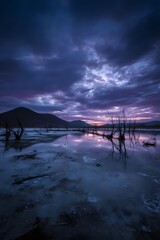 Eerie lake at dusk with silhouetted trees and dramatic clouds.