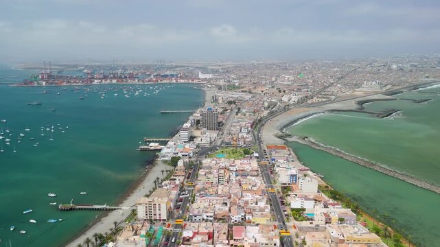 High-altitude aerial flyover reveals the unique geography of the La Punta district in Callao, Lima, a narrow peninsula with a calm harbor on one side and the Pacific Ocean on the other