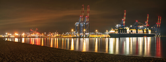 A massive container ship unloading at a container terminal in a seaport at night