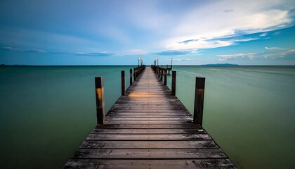 Obraz premium Serene wooden pier extending into calm sea under twilight sky