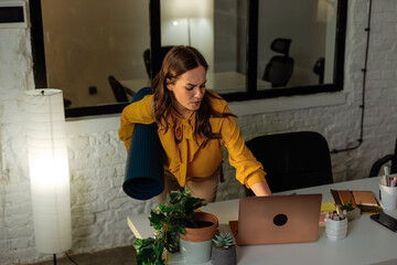 Office worker closing laptop after work and holding yoga mat
