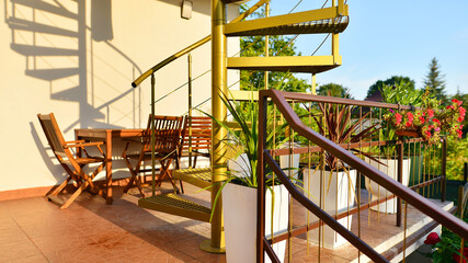 Steel spiral gold staircase on the terrace with plants and plants in pots background.