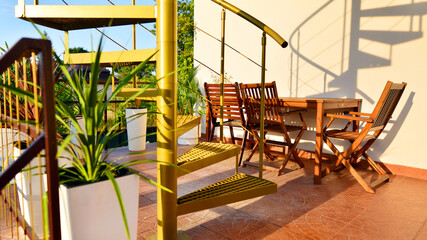 Steel spiral gold staircase on the terrace with plants and plants in pots background.
