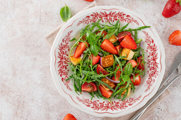 Healthy salad with strawberries, tomatoes, arugula, halloumi cheese and basil on a plate on a concrete background. Top view, copy space.