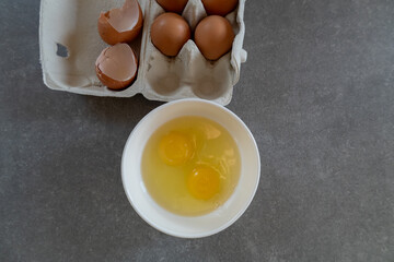 cracked eggs in bowl beside carton of brown eggs